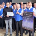 Männerchor in blauen Westen mit 1.000 Euro Scheck und Plakat des Weihnachtskonzertes bei der Scheckübergabe an den Zweiten Vorsitzenden des Kirchengemeinderates