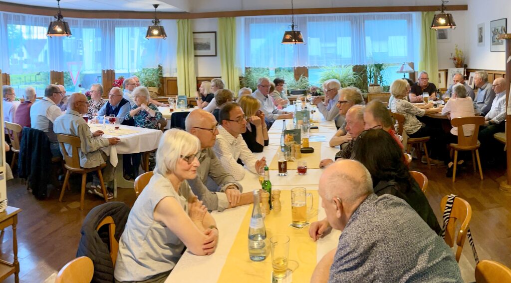 Die Sänger und ihre Frauen sitzen im Gasthaus Stadtwirten an Tischen im Gespräch vertieft.