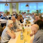 Die Sänger und ihre Frauen sitzen im Gasthaus Stadtwirten an Tischen im Gespräch vertieft.